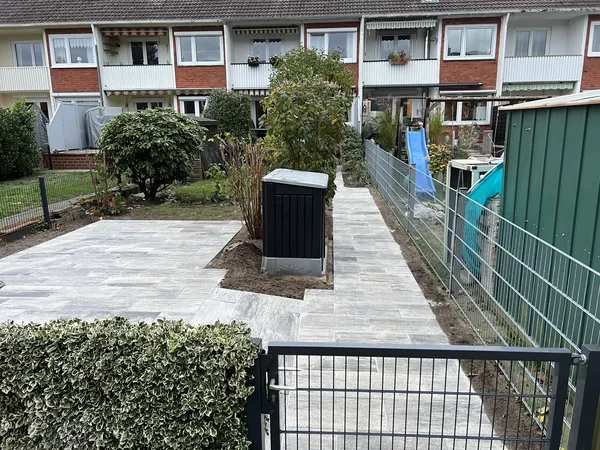 Neu gepflasterte Terrassenfläche und Plattenweg entlang des Zauns zum Reihenhaus, eingefasst von Hecke und Beeten