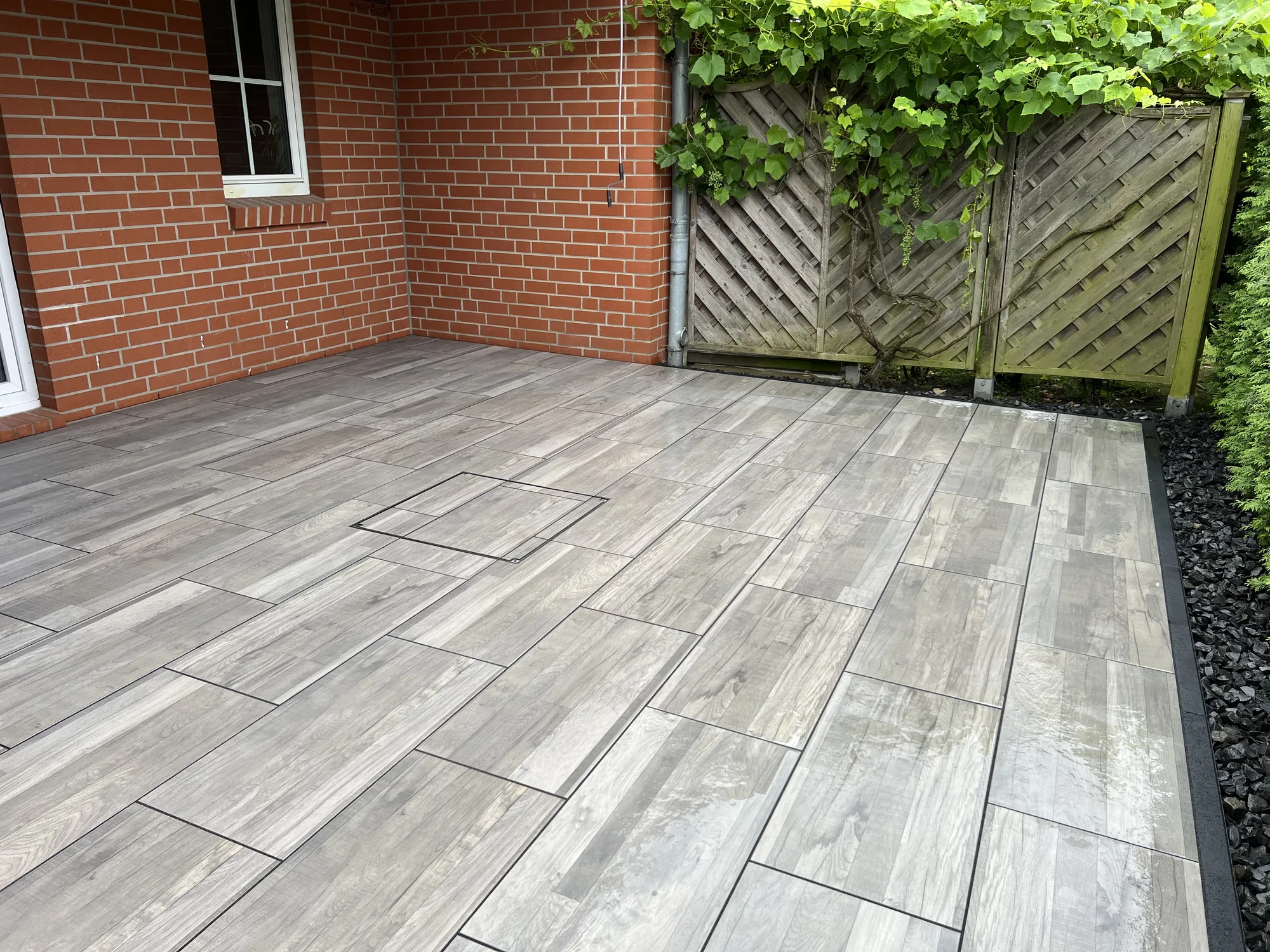 Neu verlegte Terrassenplatten in Holzoptik an der Klinkerfassade, eingefasst mit dunklem Ziersplitt